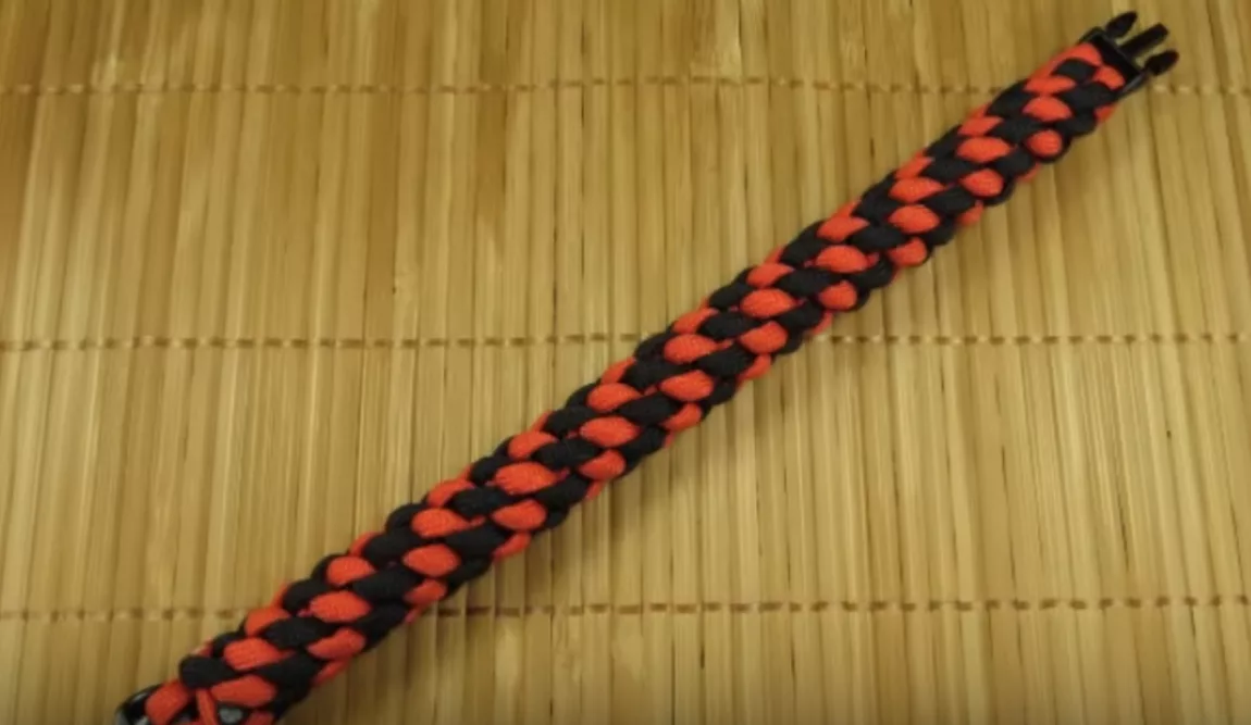 Screenshot 20260708 at 124037 AM Explore Magazine Red and black braided paracord bracelet on a light bamboo mat, close-up detail of the weave pattern.
