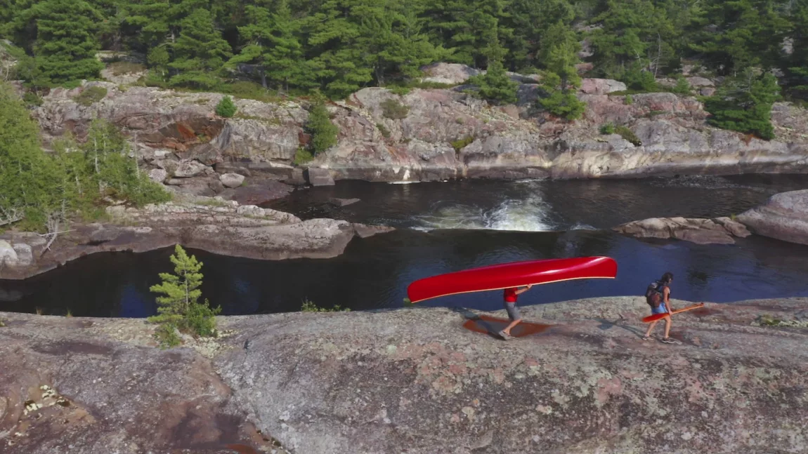 Two people carry a canoe across the rocks on the French River in Ontario, Canada. 