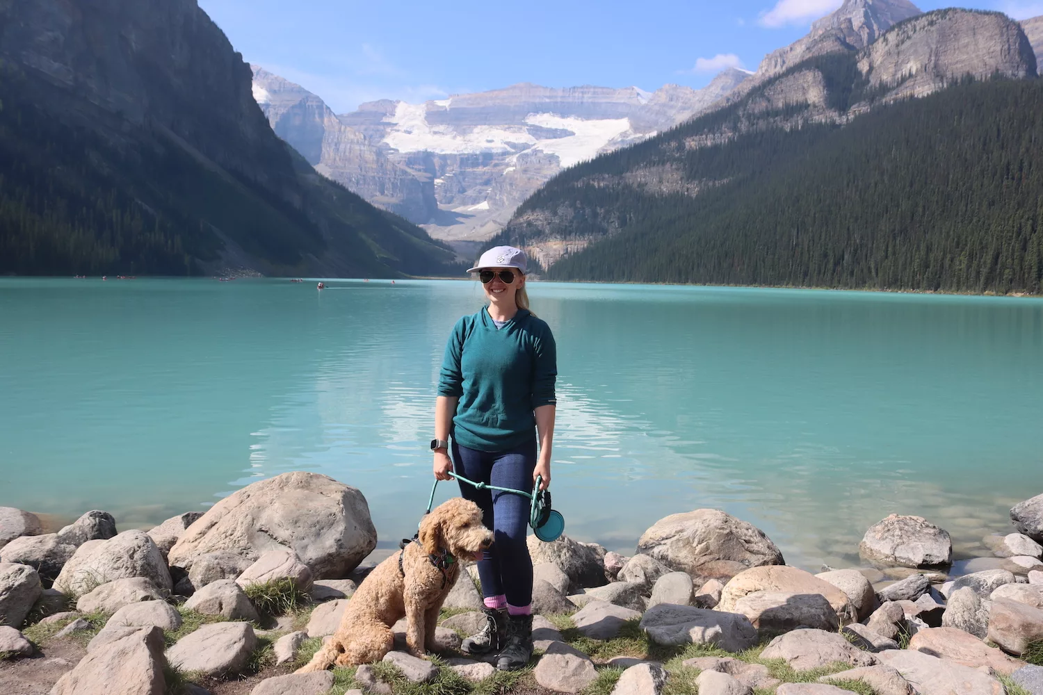 A woman stands in front of Lake Louise with her dog