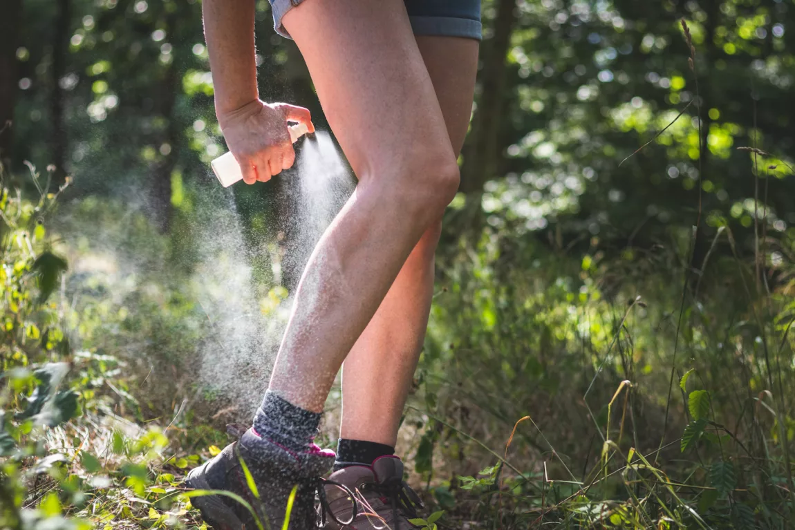 A person sprays their legs with bug spray before hiking