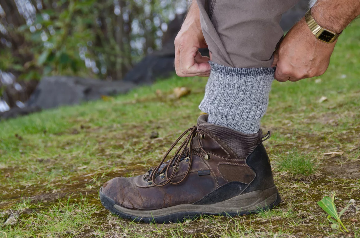 A person tucks in their hiking pant leg into their hiking boots as a tick prevention method