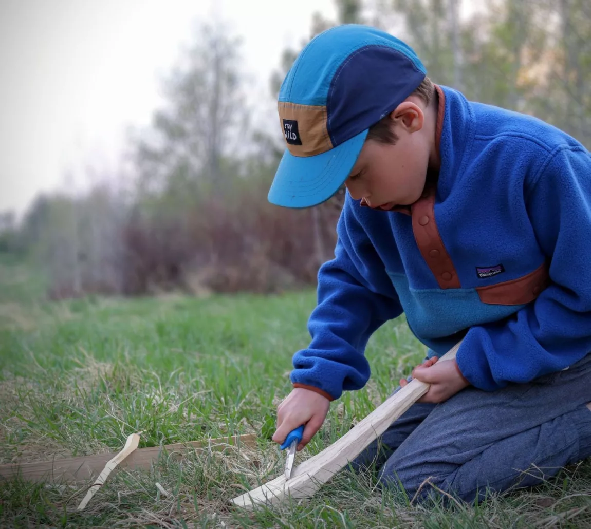 Camping trips with kids - a kid uses a knife to carve a stick