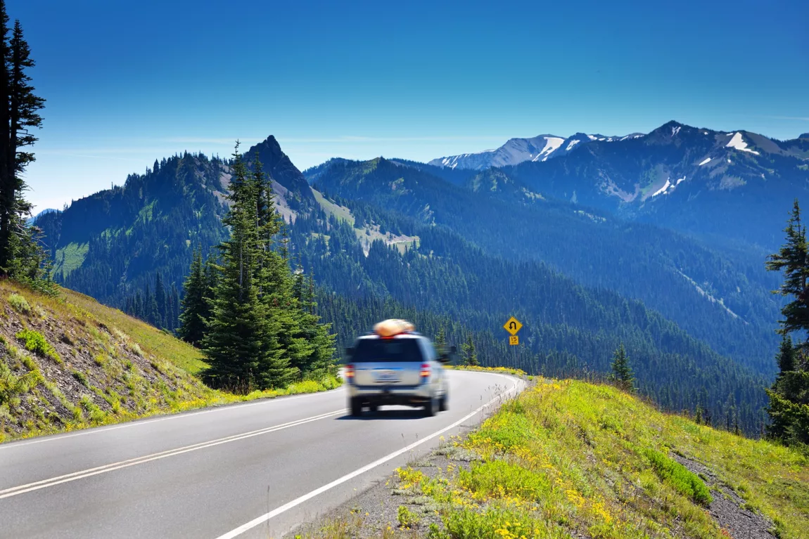 Tourist driving on the mountain road of Olympic National Park in Washington State, USA. The park features glacial snow capped mountain peaks and the scenic coastline of the Pacific Ocean. The scenic roadway around the park is a popular scenic drive. Photographed in horizontal format.