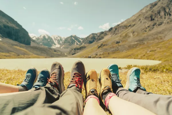 First-person view of colorful hiking boots lined up on grassy ground with a mountain valley in the background.