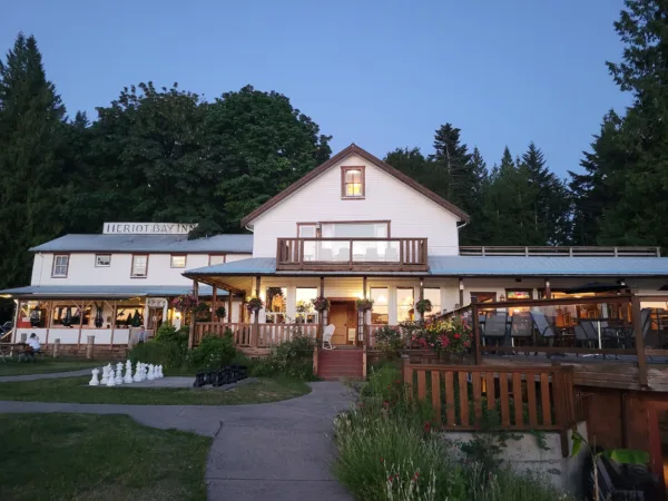1 Explore Magazine White two-story inn with a wooden balcony and outdoor seating, set against a backdrop of trees at dusk.