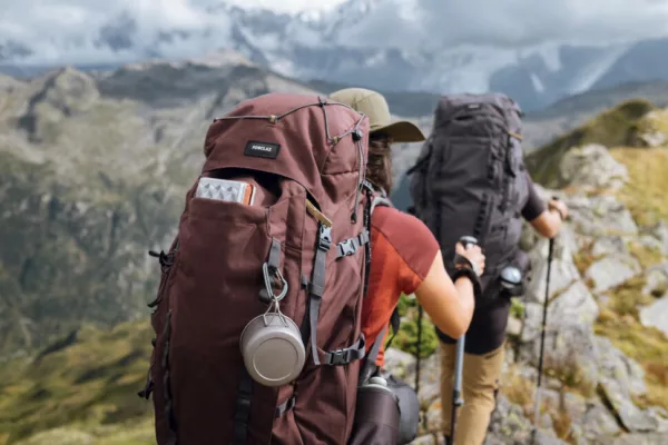 Two hikers with large backpacks on a rocky mountain trail, overlooking a valley.